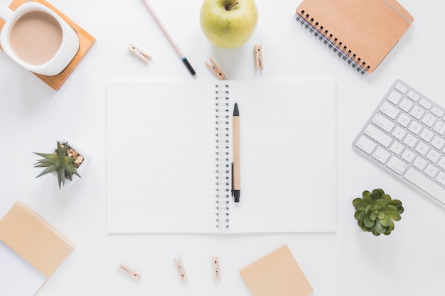 Opened notebook with pen near stationery and apple on white table