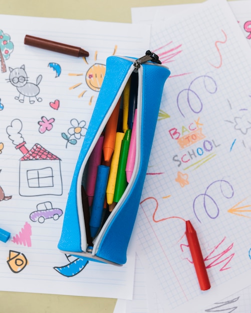 Opened pencil case with wax crayons placed on kid drawings