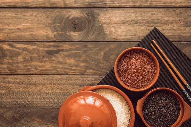 An opened pot and bowls with different type of rice grains on wooden table