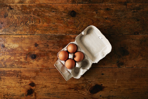 Free photo opened recyclable egg carton for six eggs containing four big brown eggs on a rough rustic brown wooden table