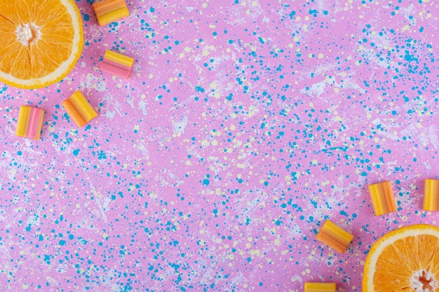 Free photo oppositely aligned orange slices surrounded with bubblegums on a colorful surface