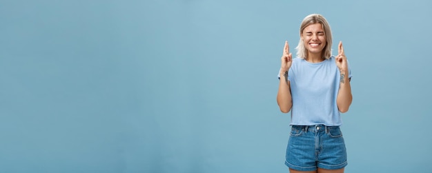 Optimistic faithful goodlooking young woman with blond hair and tattoos smiling joyfully crossing