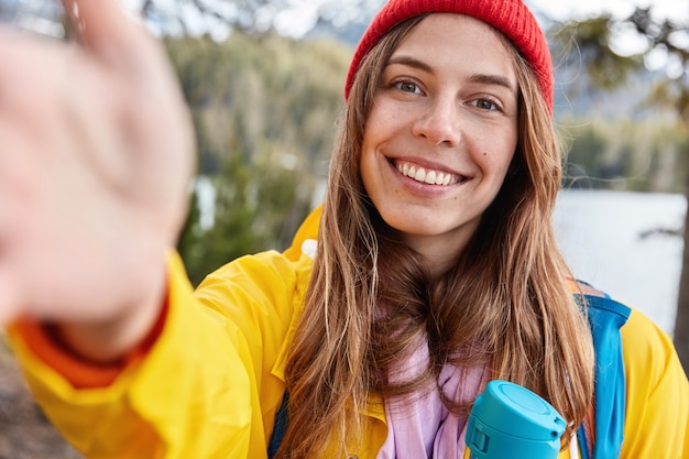 Free Photo optimistic female model has toothy smile, stretches hand as makes selfie, dressed casually