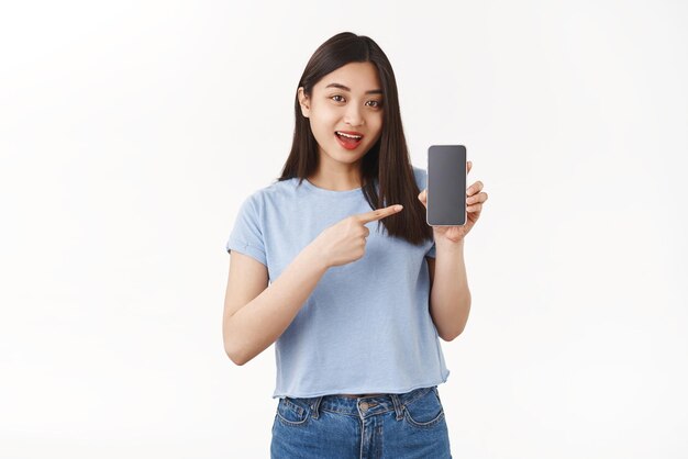 Optimistic goodlooking asian girl dark hair introduce app hold smartphone pointing cellphone screen speaking about interesting application game stand white background show social media profile