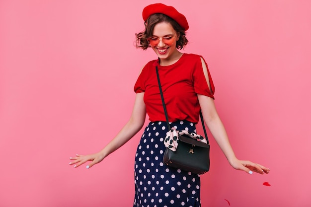 Free photo optimistic young girl wears colorful glasses dancing in studio inspired french woman in beret having fun on pink background