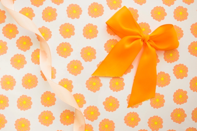 Free photo an orange bow and curled ribbon on floral gift paper