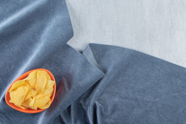 Free photo orange bowl of tasty ripple chips on stone.