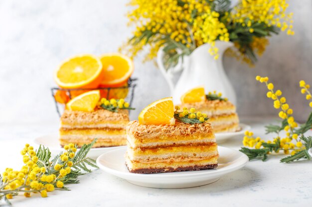 Orange cake decorated with fresh orange slices and mimosa flowers on light