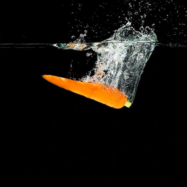 Free Photo an orange carrot falling in water splash against black background