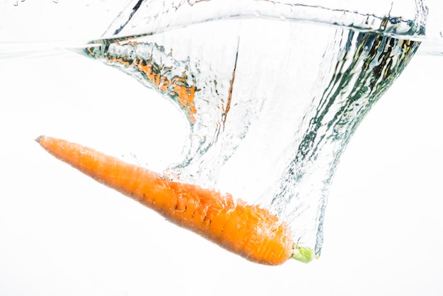 Free Photo an orange carrot splashing in the water against white background