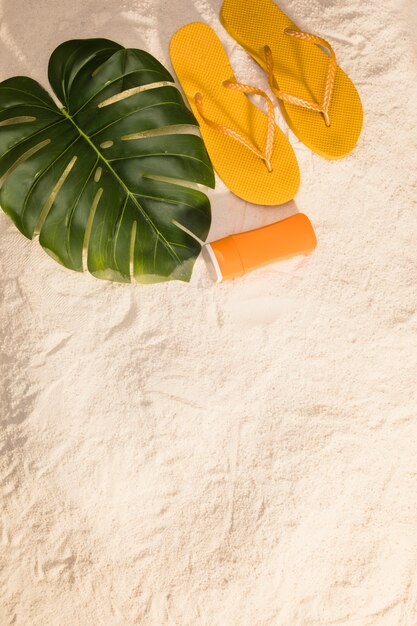 Orange flip flops and monstera leaves on beach