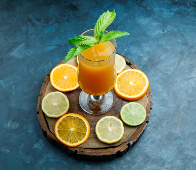 Free photo orange juice in a goblet with mint, lime, lemon, orange high angle view on grungy blue and wooden board