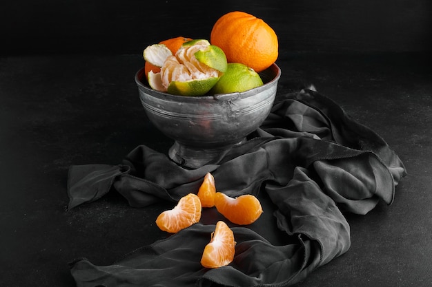 Orange mandarines in a metallic cup on black surface. 