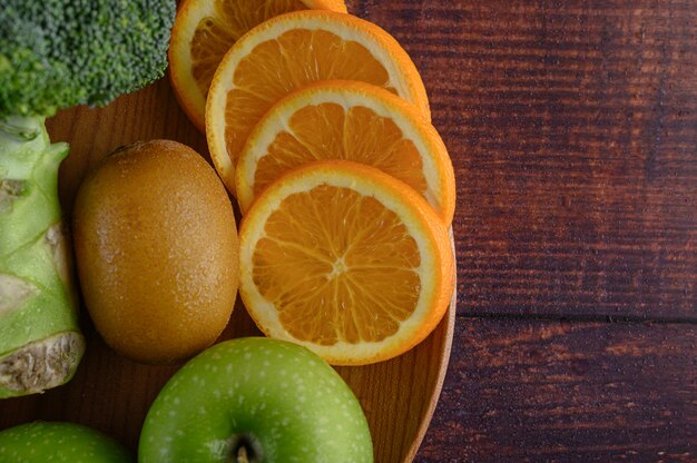 Orange pieces, apple, kiwi, and Broccoli on a wooden plate.