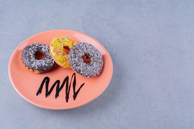 An orange plate of delicious chocolate doughnuts with sprinkles. 