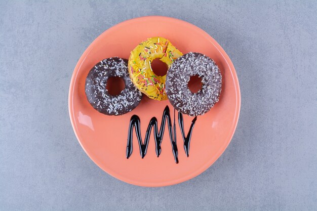 An orange plate of delicious chocolate doughnuts with sprinkles.