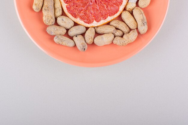 Orange plate of grapefruit slice and organic peanuts on white background. High quality photo