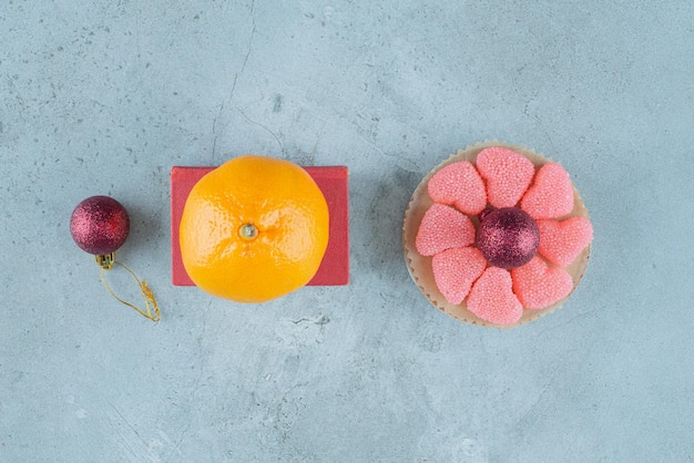 Orange on a red box next to a small platter of marmelades around a decorative ball on marble.