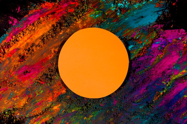 Free photo orange round frame on colorful holi color powder over the black backdrop