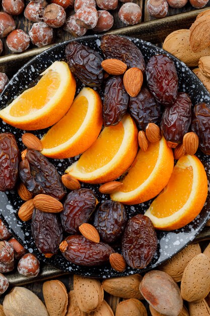 Orange slices with dates, almonds and nuts in a plate on copper tray