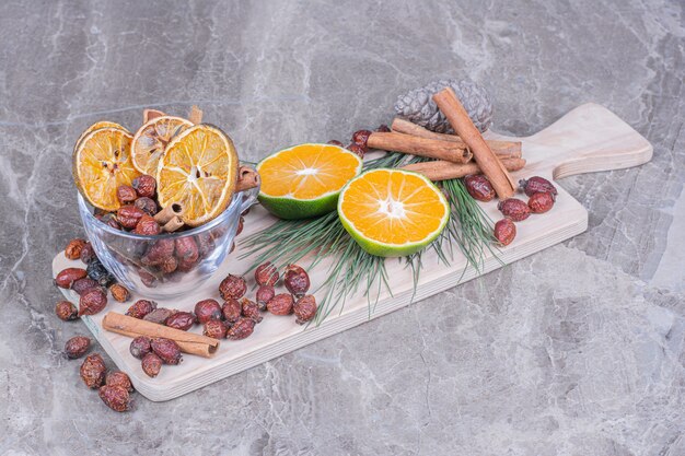 Orange slices with dry hips and cinnamon sticks on a wooden platter