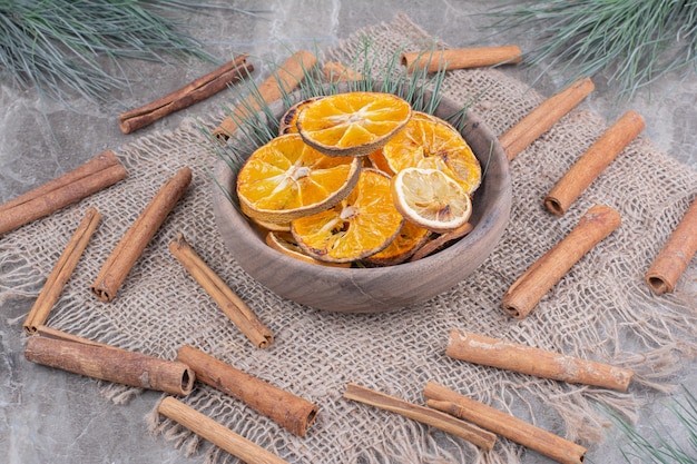 Orange slices in a wooden cup with cinnamon sticks around