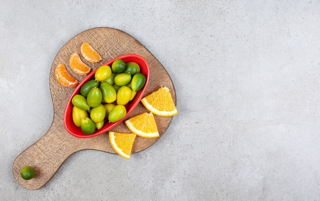 Free photo orange and tangerine slices whit bowl of kumquats on wooden board.