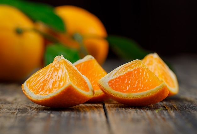 Oranges with slices and branch side view on black and wooden table