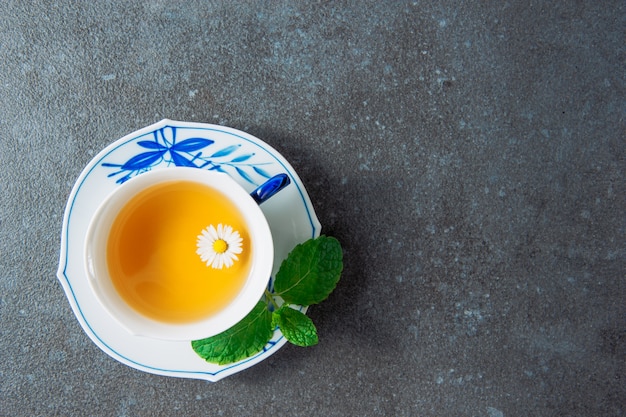 Organic chamomile tea in a cup and saucer with green leaves top view on a grey stucco background