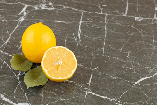 Organic half cut and whole lemons on grey stone.