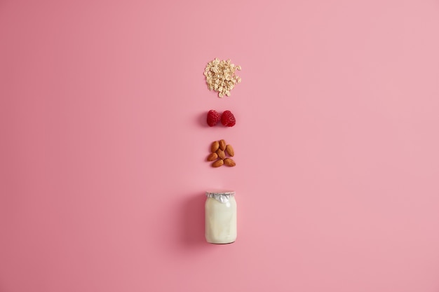 Organic nutrition, healthy breakfast concept. Yoghurt or vegan milk in jar, oatmeal cereals, raspberry and almond nut for making tasty snack. Natural ingredients. Vegetearian meal and dieting