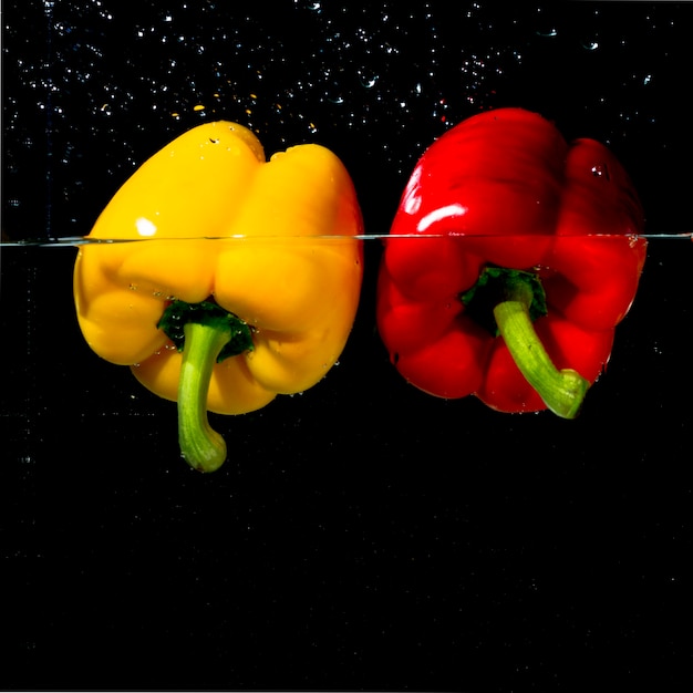 Free photo organic red and yellow bell pepper floating on clear water against black background