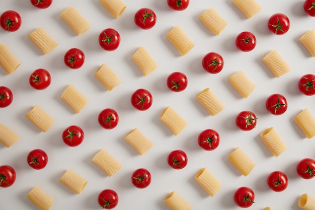 Organic rigatoni pasta and red cherry tomatoes arranged in rows on white  background. Creative layout for menu. Food concept. Healthy dry macaroni pasta. Above shot, view from overhead