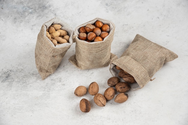 Free photo organic shelled hazelnuts, peanuts and walnuts in sackcloth on marble table.