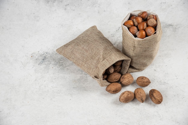 Organic shelled hazelnuts and walnuts in sackcloth on marble table. 