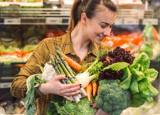 Organic vegetables close up. Beautiful young woman shopping in a supermarket and buying fresh organic vegetables