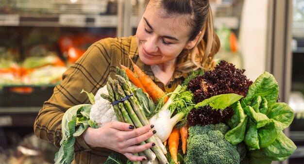 Organic vegetables close up. Beautiful young woman shopping in a supermarket and buying fresh organic vegetables