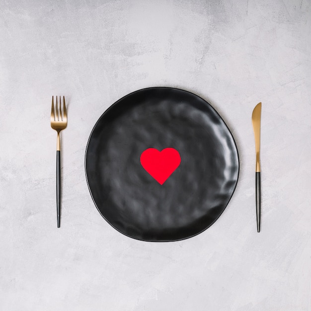 Ornament heart on black plate between cutlery 