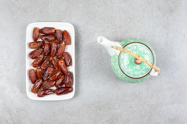 Ornate teapot next to a plate of fresh dates on marble background. High quality illustration