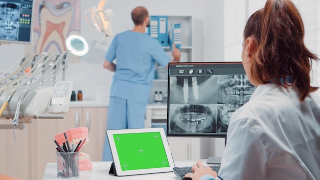 Free photo orthodontist using horizontal green screen on tablet for oral care and dentistry. woman working as dentist with chroma key and isolated mockup template while looking at teeth scan