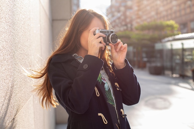 Free Photo outdoor autumn smiling lifestyle portrait of pretty young woman, having fun in the city with camera, travel photo of photographer. making pictures in hipster style.