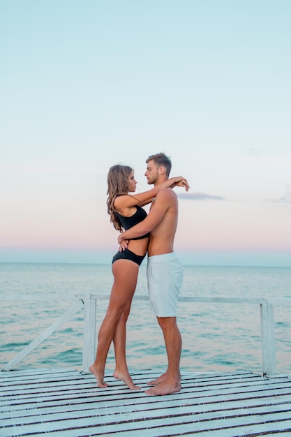 Outdoor close up fashion portrait of pretty sexy couple in love hugs on amazing tropical beach wearing stylish swimwear