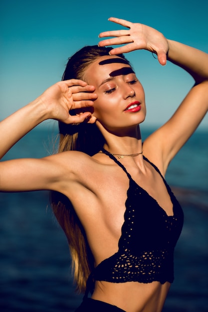 Free photo outdoor fashion portrait of fit tan perfect woman in stylish black knitted swimwear posing on the beach.