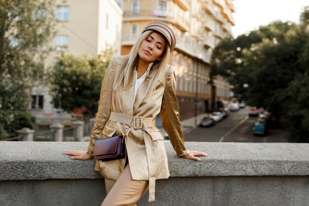 Outdoor image of elegant european woman walking in autumn city . Beige cap and jacket. stylish accessories. 
