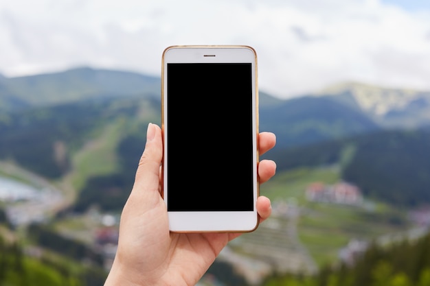 Outdoor image of one hand holding and showing white smartphone with blank black desktop screen