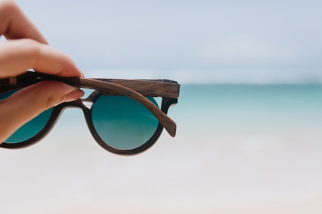 Free photo outdoor photo of ocean with female hand on foreground. woman holding summer sunglasses on sea.