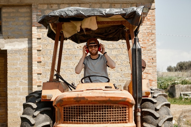 Outdoor picture of handsome cheerful young bearded farmer wearing sunglasses