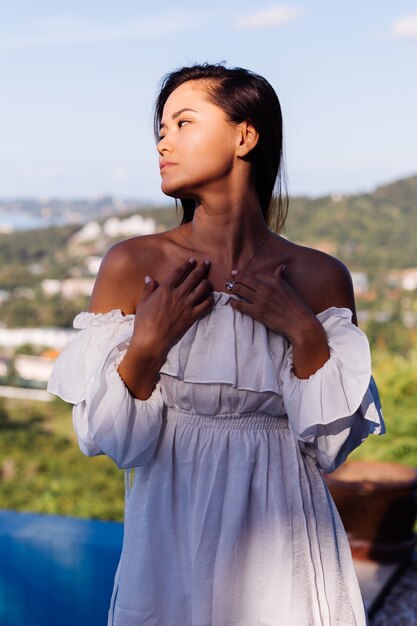 Outdoor portrait of asian woman in white dress wearing necklace.