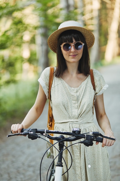 Free photo outdoor portrait of attractive young brunette in a hat on a bicycle.