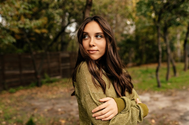 Outdoor portrait of charming pretty european woman with long wavy hair wearing green sweater walking in the park